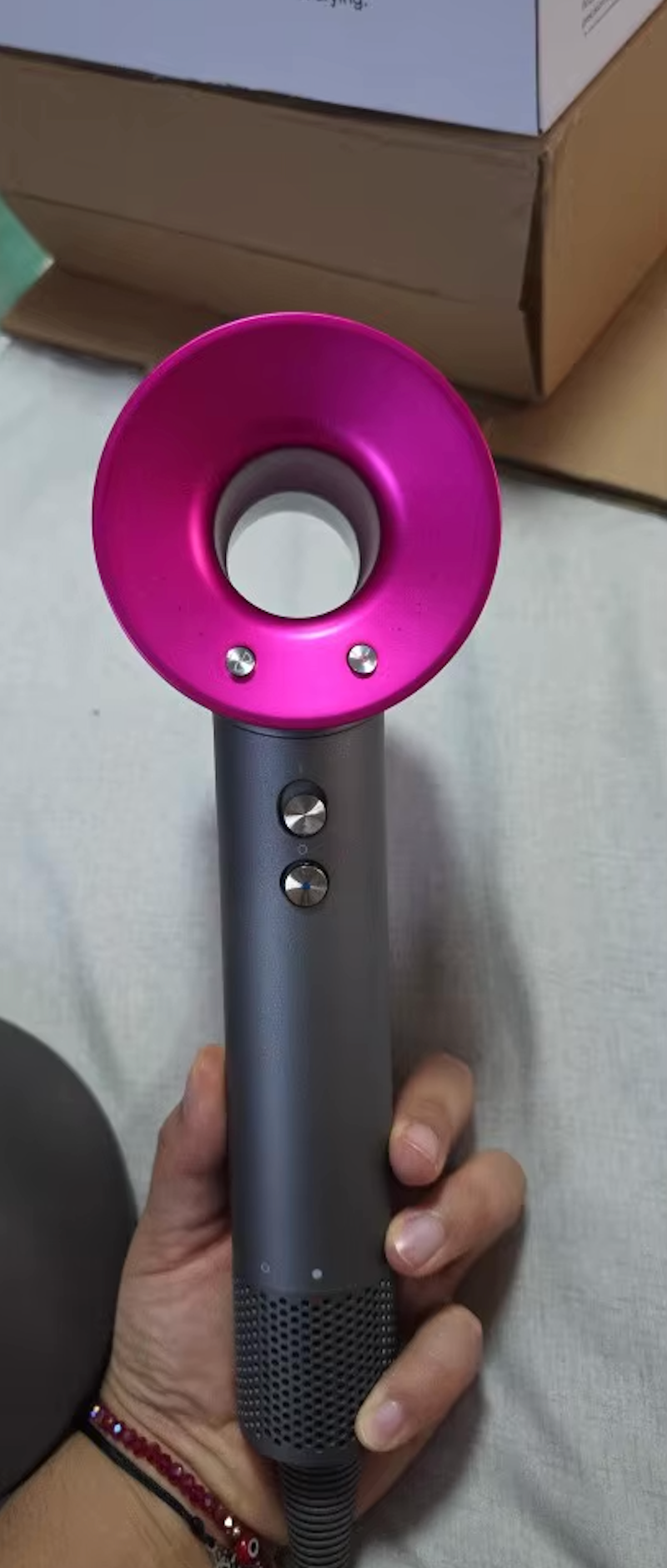 StyloAir hårfön i grått med rosa ring, visad i hand framför produktförpackning.