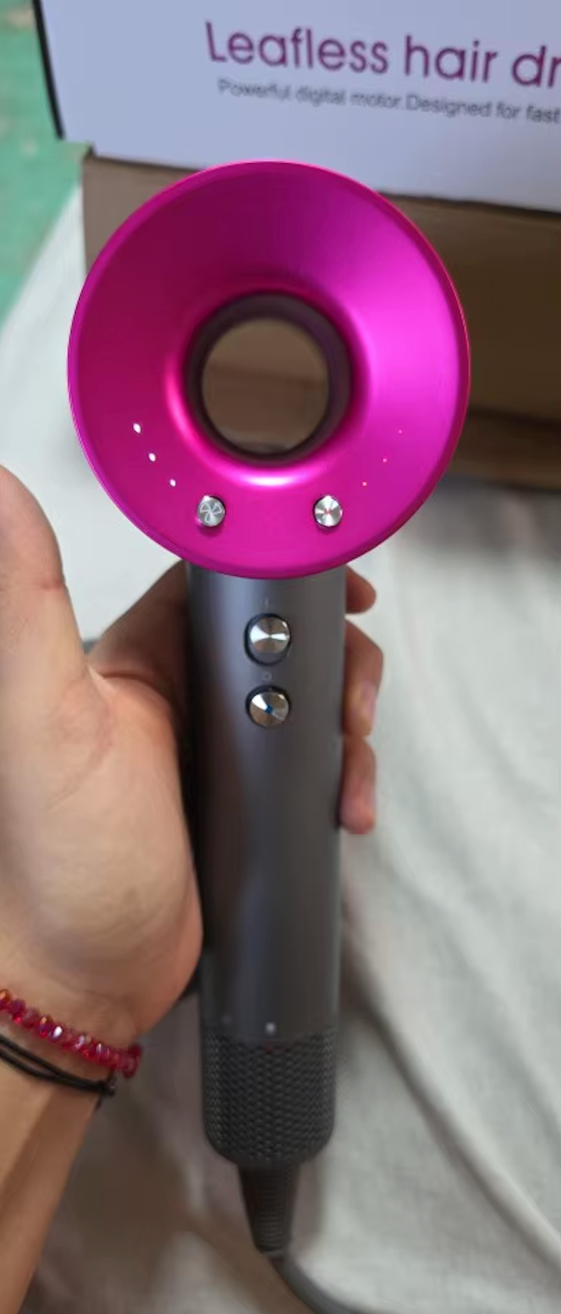 StyloAir hårfön i grått med rosa ring, visad i hand framför produktförpackning.